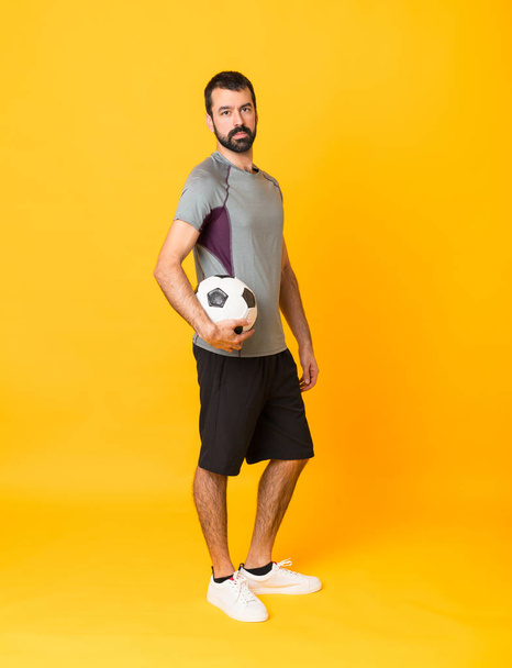 Full-length shot of man over isolated yellow background with soccer ball - Foto, immagini