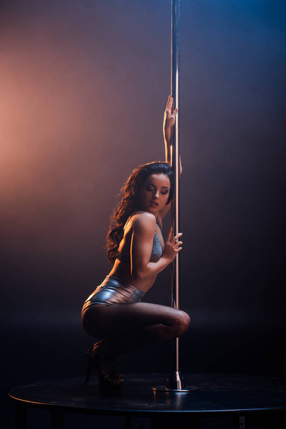 attractive stripper in underwear sitting near pole on blue and orange  - Fotó, kép