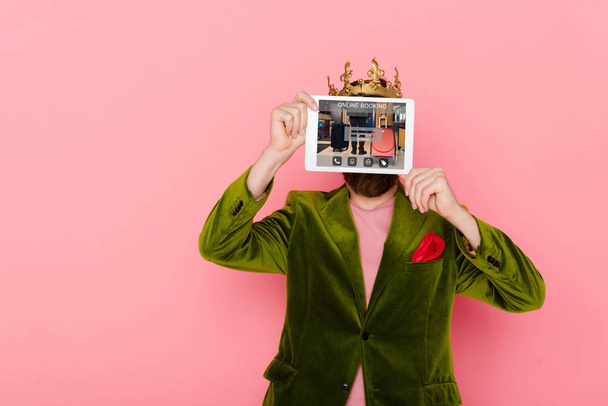 man with crown holding digital tablet with online booking isolated on pink - Foto, Bild