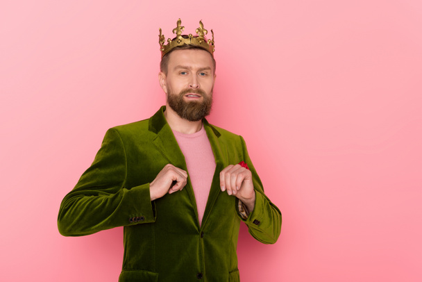handsome man with crown in velour jacket looking at camera on pink background  - Photo, Image