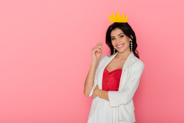 smiling woman holding paper crown looking at camera on pink background  - Foto, Imagen
