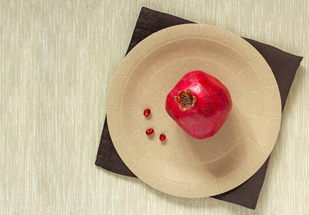 A whole bright red ripe pomegranate with three seeds on a paper plate - Zdjęcie, obraz