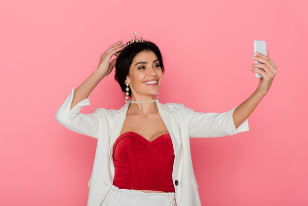 smiling woman with crown taking selfie on pink background  - Photo, Image