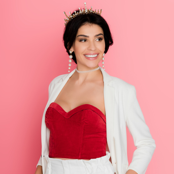 smiling woman with crown looking away on pink background  - Foto, imagen