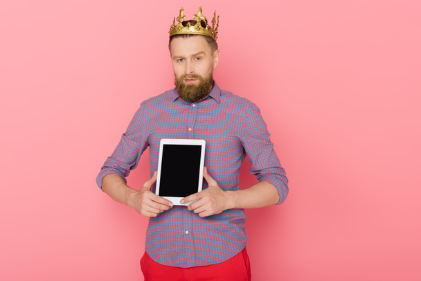 Mann mit Krone hält digitales Tablet auf rosa Hintergrund  - Foto, Bild