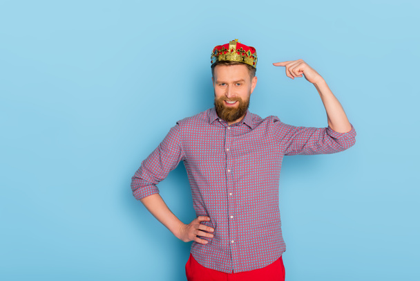 smiling man pointing with finger at crown on blue background  - Photo, Image