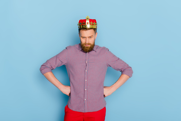 naštvaný muž s korunou při pohledu na kameru na modrém pozadí  - Fotografie, Obrázek