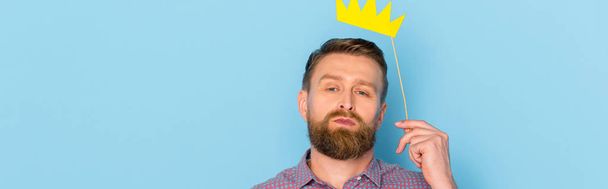 панорамный снимок человека, держащего бумажную корону на синем фоне
  - Фото, изображение