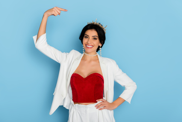 smiling woman pointing with finger at crown on blue background  - Foto, immagini