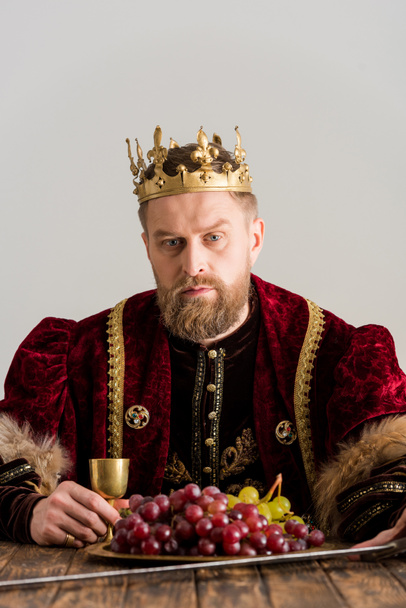 king with crown sitting at table isolated on grey - Photo, Image