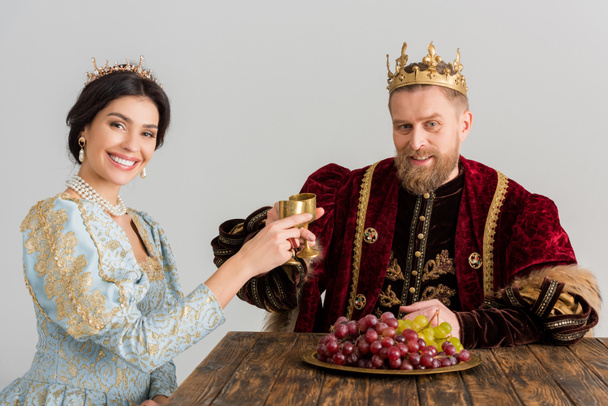 smiling queen and king with crowns clinking with cups isolated on grey - Fotoğraf, Görsel