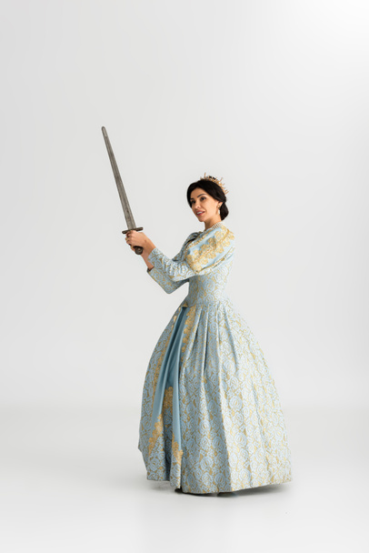 ελκυστική βασίλισσα με στέμμα κρατώντας σπαθί σε γκρι φόντο  - Φωτογραφία, εικόνα