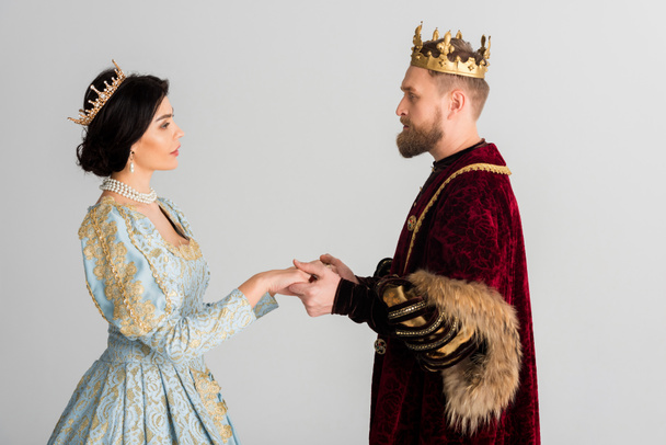 boční pohled na královnu a krále s korunami držícími se za ruce izolované na šedi  - Fotografie, Obrázek