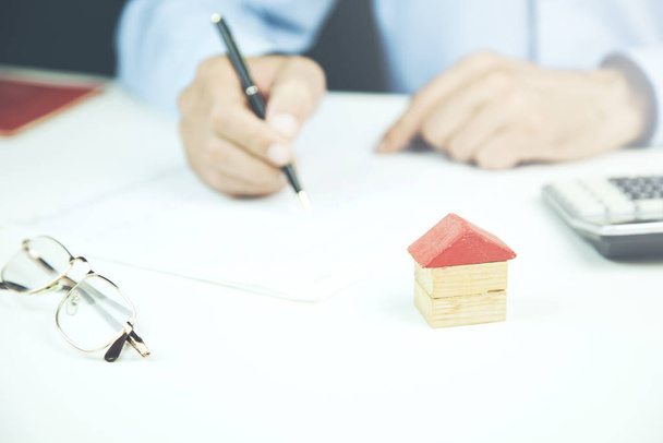 Un homme d'affaires signe un contrat derrière un modèle architectural maison
 - Photo, image