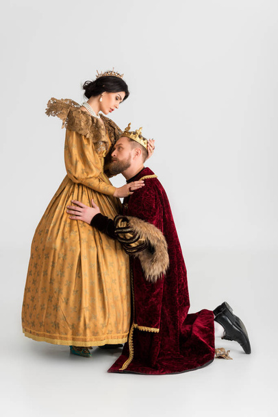 Seitenansicht des Königs mit Krone umarmt attraktive Königin auf grauem Hintergrund  - Foto, Bild