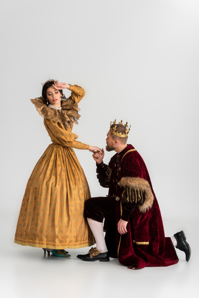 király koronával kéz a kezében megdöbbent királynő szürke háttér  - Fotó, kép