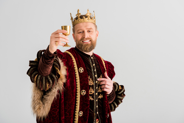 sonriente rey con corona sosteniendo copa aislada en gris
 - Foto, imagen