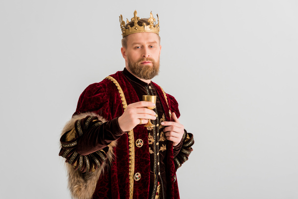 guapo rey con corona sosteniendo la taza y mirando a la cámara aislada en gris
 - Foto, imagen