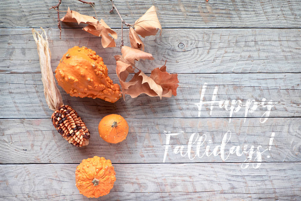 秋の葉とカボチャ、テキスト"ハッピーホリデー" 。フラットレイアウト、木製テーブルの上にオレンジのカボチャ、トウモロコシの穂軸と乾燥葉の上ビュー - 写真・画像