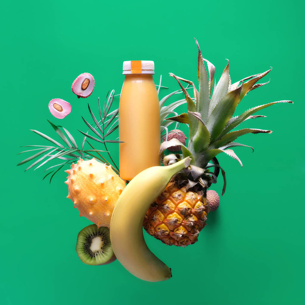 Assortment of tropical fruits around smoothie bottle on green ba - Фото, зображення