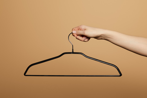 cropped view of woman holding empty hanger isolated on beige - Fotó, kép