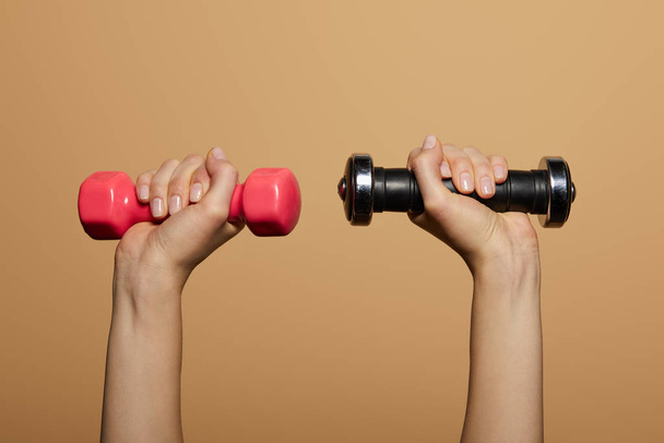cropped view of woman holding dumbbells isolated on beige - Фото, изображение