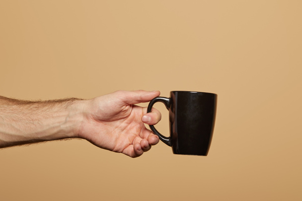 cropped view of man holding black mug isolated on beige - Фото, изображение