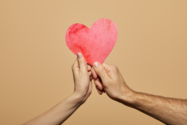 vista recortada del hombre y la mujer sosteniendo el corazón rojo aislado en beige
 - Foto, imagen