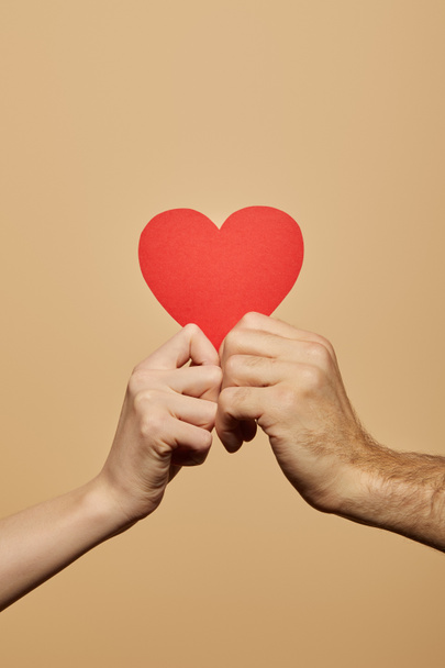 cropped view of man and woman holding red heart isolated on beige - Photo, image