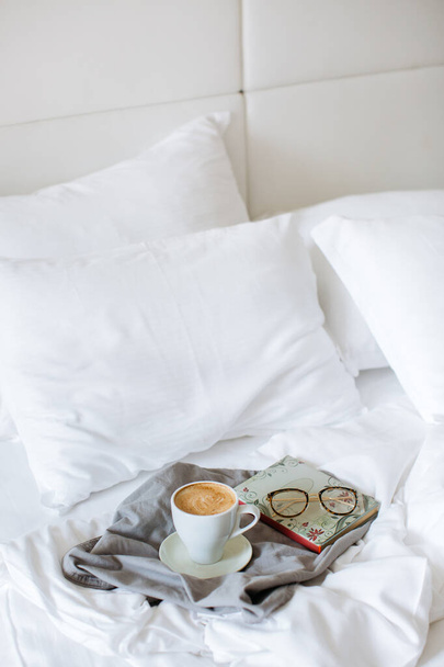biały kubek rano pyszna kawa z książką i szklanki na białym tle łóżka - Zdjęcie, obraz