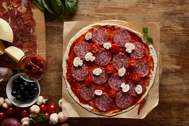 Top view of pizza with salami, mushrooms and tomato sauce on wooden background - Foto, Imagem