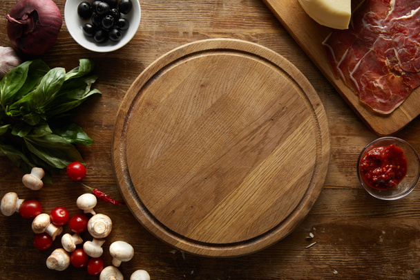 Top view of ingredients for pizza around cutting board on wooden background - Foto, Bild