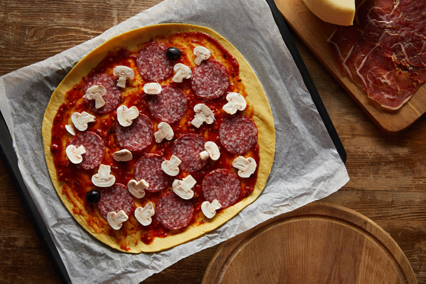Top kilátás ízletes pizza szalámi és gomba pergamen papír fa háttér  - Fotó, kép