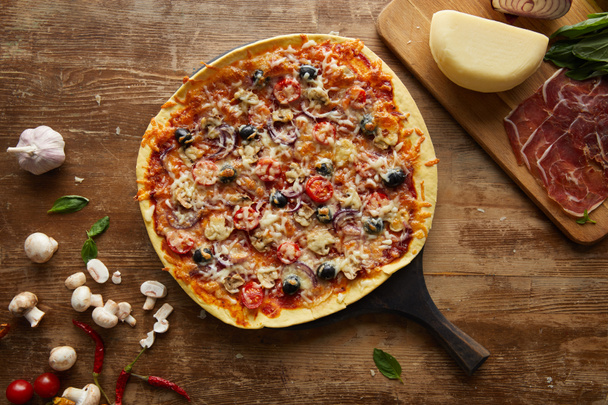 Vista superior de pizza saborosa e alho, presunto, cogumelos, parmesão, pimentão e manjericão em fundo de madeira
 - Foto, Imagem