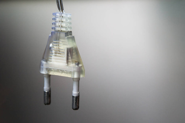Enchufe europeo eléctrico transparente colgado en un cordón sobre un fondo de gradiente gris. Vista de cerca. Enfoque selectivo
 - Foto, imagen