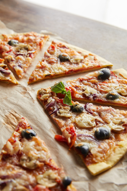 cut delicious italian pizza with olives on baking paper on wooden table - Foto, Imagen