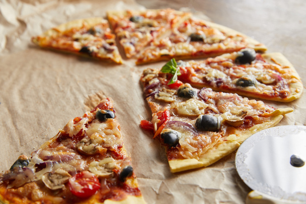 close up view of cut delicious italian pizza with olives on baking paper with pizza knife on wooden table - Φωτογραφία, εικόνα