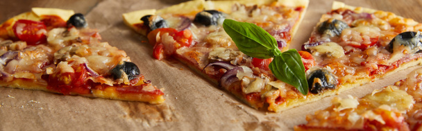 leckere italienische Pizza mit Oliven und Basilikum auf Backpapier auf Holztisch schneiden, Panoramaaufnahme - Foto, Bild