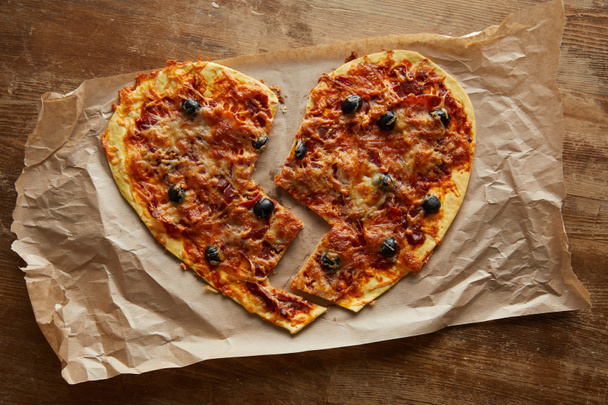 top view of delicious italian pizza in broken heart shape on baking paper on wooden table - Photo, Image