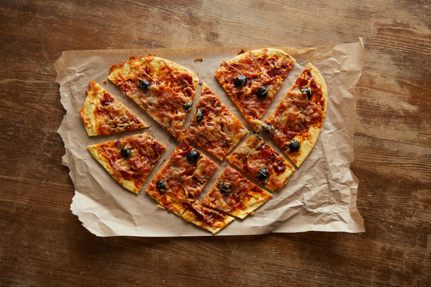 vue de dessus de délicieuses pizzas italiennes en forme de coeur coupées en morceaux sur du papier cuisson sur une table en bois
 - Photo, image