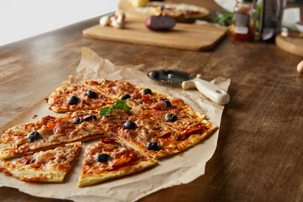 deliciosa pizza italiana em forma de coração cortada em pedaços em papel manteiga perto de faca de pizza e ingredientes em mesa de madeira
 - Foto, Imagem