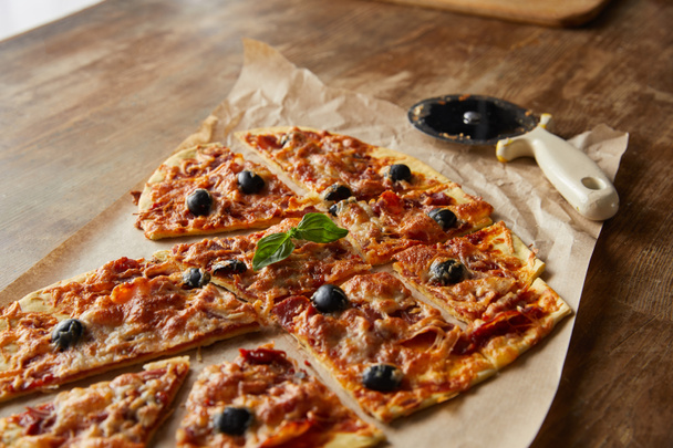 delicious italian pizza in heart shape cut into pieces on baking paper near pizza knife on wooden table - Valokuva, kuva