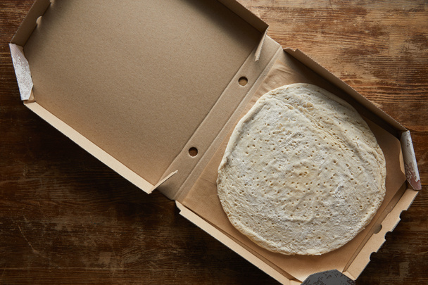 top view of raw dough in pizza box on wooden table - Fotó, kép