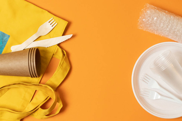 Plastový kelímek, talíř, vidličky, papírové kelímky, přírodní bavlněná žlutá taška, vidličky a nože na oranžovém pozadí. Konfrontace. Ekologická katastrofa - Fotografie, Obrázek
