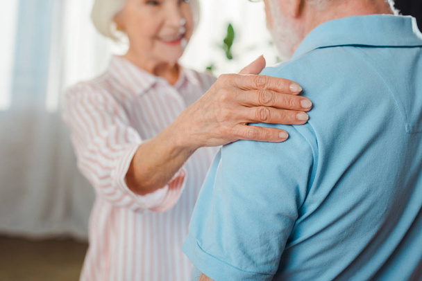 Selective focus of smiling senior woman touching husband by shoulder at home - Photo, Image
