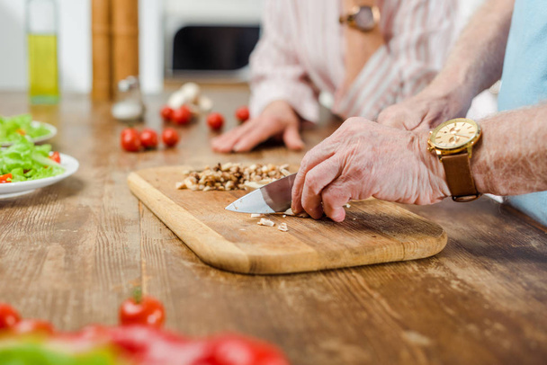 Vista recortada del hombre mayor cortando setas junto a la esposa en la cocina
 - Foto, Imagen