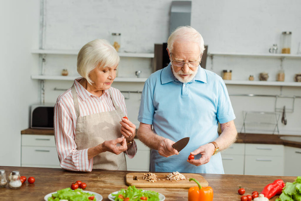 Seniorenpaar schneidet Gemüse beim gemeinsamen Kochen in Küche  - Foto, Bild