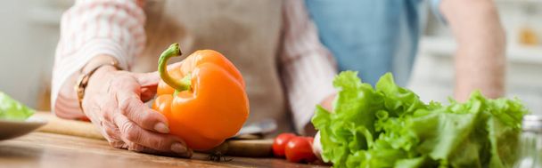 Cropped view of woman holding bell pepper while cooking by man in kitchen, panoramic shot - Foto, Imagen