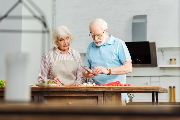 Enfoque selectivo de pareja de ancianos cocinando juntos en la mesa de la cocina
 - Foto, Imagen