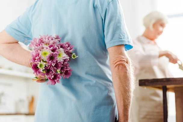 foyer sélectif de l'homme cachant bouquet avec femme par table de cuisine à l'arrière-plan
 - Photo, image